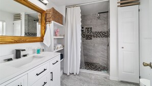 A bathroom with a white vanity, a large mirror, a shower with a glass door, and a white door. - Elegant & Cozy 3-Bedroom Home in Ocala – Perfect for a Relaxing Stay (Ocala)
