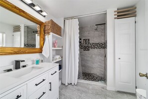 Ein Badezimmer mit weißem Waschtisch, einem großen Spiegel, einer Dusche mit Glastür und einer weißen Tür.