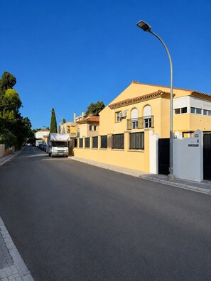 A street with a white van parked on the side, a clear blue sky, and buildings with balconies and a gated entrance. - Montemar | 8-minute walk to the beach (Torremolinos)