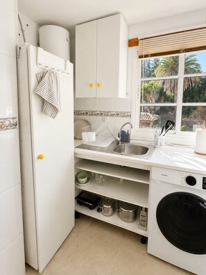 A compact kitchen with a built-in washing machine, a sink, and a window with a view of greenery. - Montemar | 8-minute walk to the beach (Torremolinos)