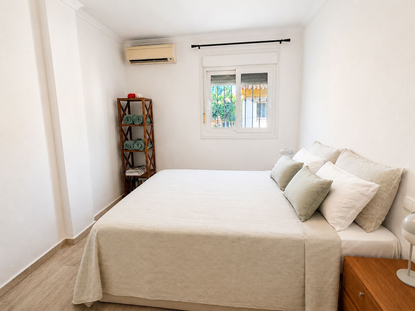 Een slaapkamer met een bed, een raam met uitzicht, een houten plank met handdoeken en een airconditioning.
