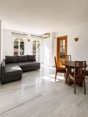 A spacious living area with a grey sectional sofa, a wooden dining table with chairs, and large windows allowing natural light. - Montemar | An 8-minute walk from the beach (Torremolinos)