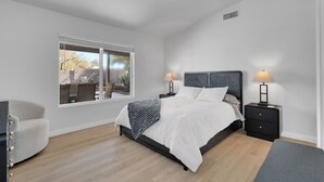 A bedroom with a bed, bedside tables, a chair, and a window. - Remodeled 3BR Home With Private Pool Near Northwest Medical Center And I-10 (Tucson)