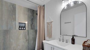 A modern bathroom with a white vanity, a large mirror, and a shower area. - Remodeled 3BR Home With Private Pool Near Northwest Medical Center And I-10 (Tucson)