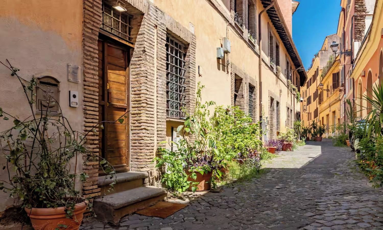 A narrow cobblestone street flanked by buildings with traditional architecture, including wooden shutters and stone walls.