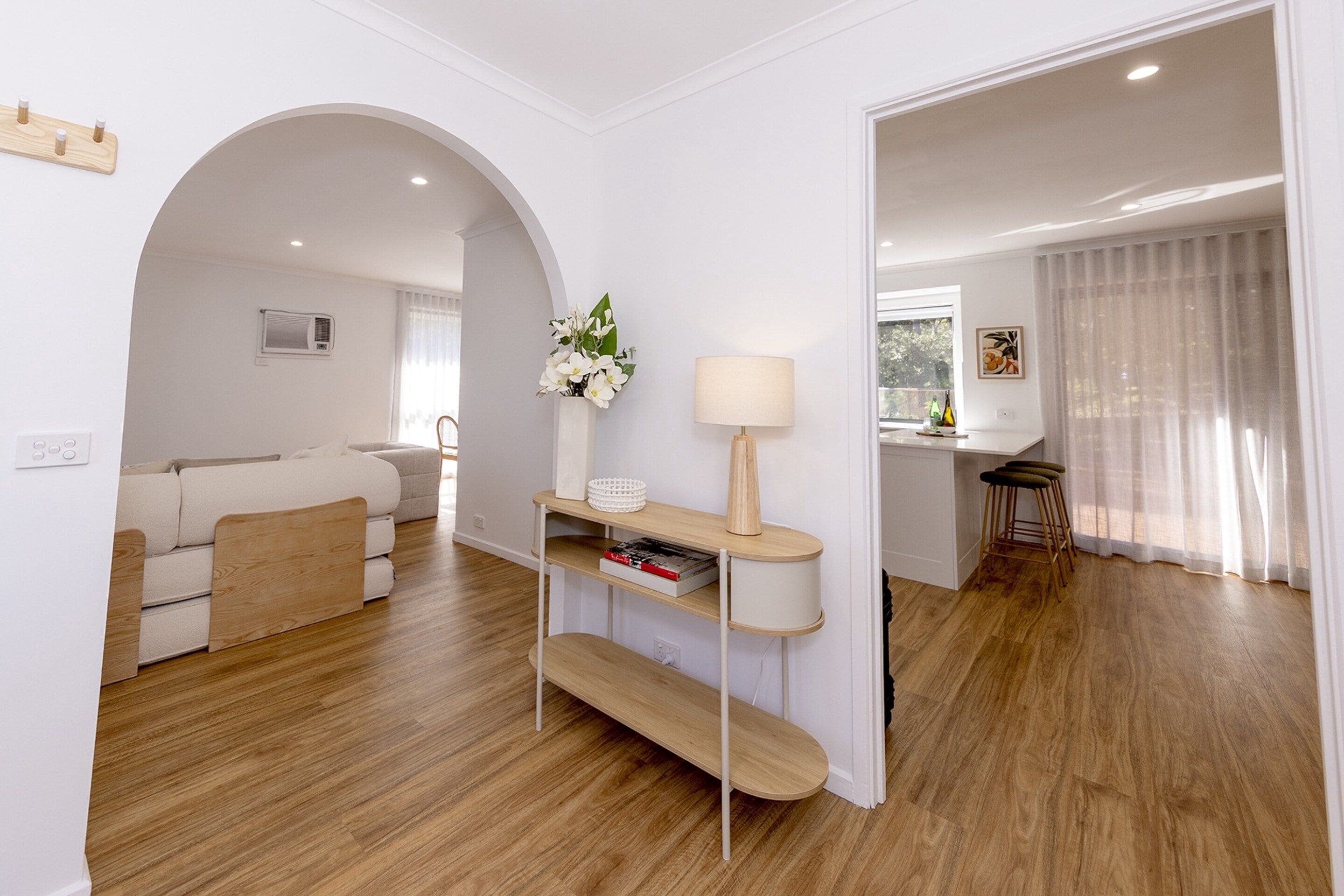 Sala de estar moderna com sofá, mesa de centro e abajur. Há um corredor dando acesso a outro quarto.