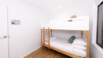 Quarto com beliche, escada de madeira, roupa de cama branca e janela.