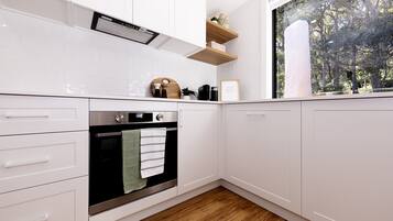 Una cocina moderna con armarios blancos, horno integrado y ventana con vista a un bosque.