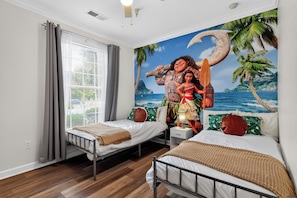 Ein Schlafzimmer mit zwei Betten, einem Fenster mit Jalousien, einem Wandgemälde mit tropischer Szenerie und Holzboden.