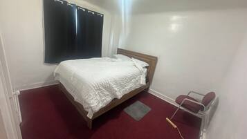 Un dormitorio con cama, ventana con cortinas, radiador y mesita de noche.