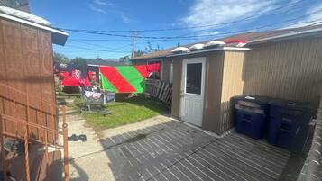 Un patio trasero residencial con un cobertizo pequeño, un tendedero y un carrito metálico con objetos.