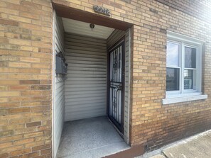 A brick building with a closed garage door, a window with a sign, and a small concrete step leading to the door.