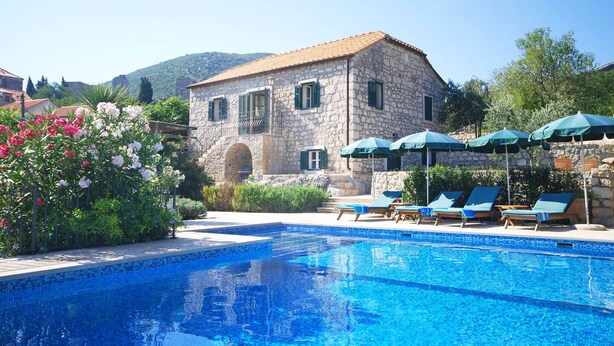 Un edificio de piedra con piscina, sillas de descanso y sombrillas.