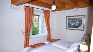 Un dormitorio con cama, cortinas, ventana, un cuadro y una lámpara.