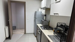Een praktische keuken met een koelkast, fornuis en vaatwasser. Een deur leidt naar een andere kamer.