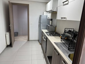 Une cuisine compacte équipée d’un réfrigérateur, d’une cuisinière et d’un lave-vaisselle. Une porte donne accès à une autre pièce.