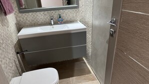Een badkamer met een wit toilet, een wastafel met spiegel erboven en een deur aan de rechterkant.
