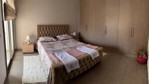 Een slaapkamer met een groot bed, een kledingkast, een nachtkastje en een raam met gordijnen.