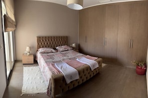 Une chambre à coucher avec un grand lit, une armoire, une table de chevet et une fenêtre avec des rideaux.