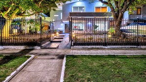 Área residencial murada com um caminho pavimentado que leva a um edifício moderno de dois andares, com grandes janelas e garagem visível.