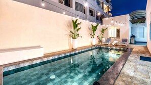 Piscina com borda azulejada, rodeada por espreguiçadeiras e plantas em vasos.