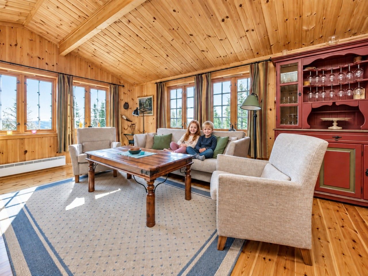 A cozy living room with a wooden ceiling, a sofa, a coffee table, and a cabinet with glassware.