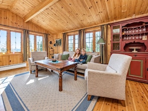 A cozy living room with a wooden ceiling, a sofa, a coffee table, and a cabinet with glassware. - Trysilfjell Ski in Ski out Family Cabin (Trysil)