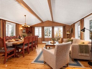 A spacious living room with a high ceiling, wooden beams, a dining area with a table set for four, and a sofa. - Trysilfjell Ski in Ski out Family Cabin (Trysil)