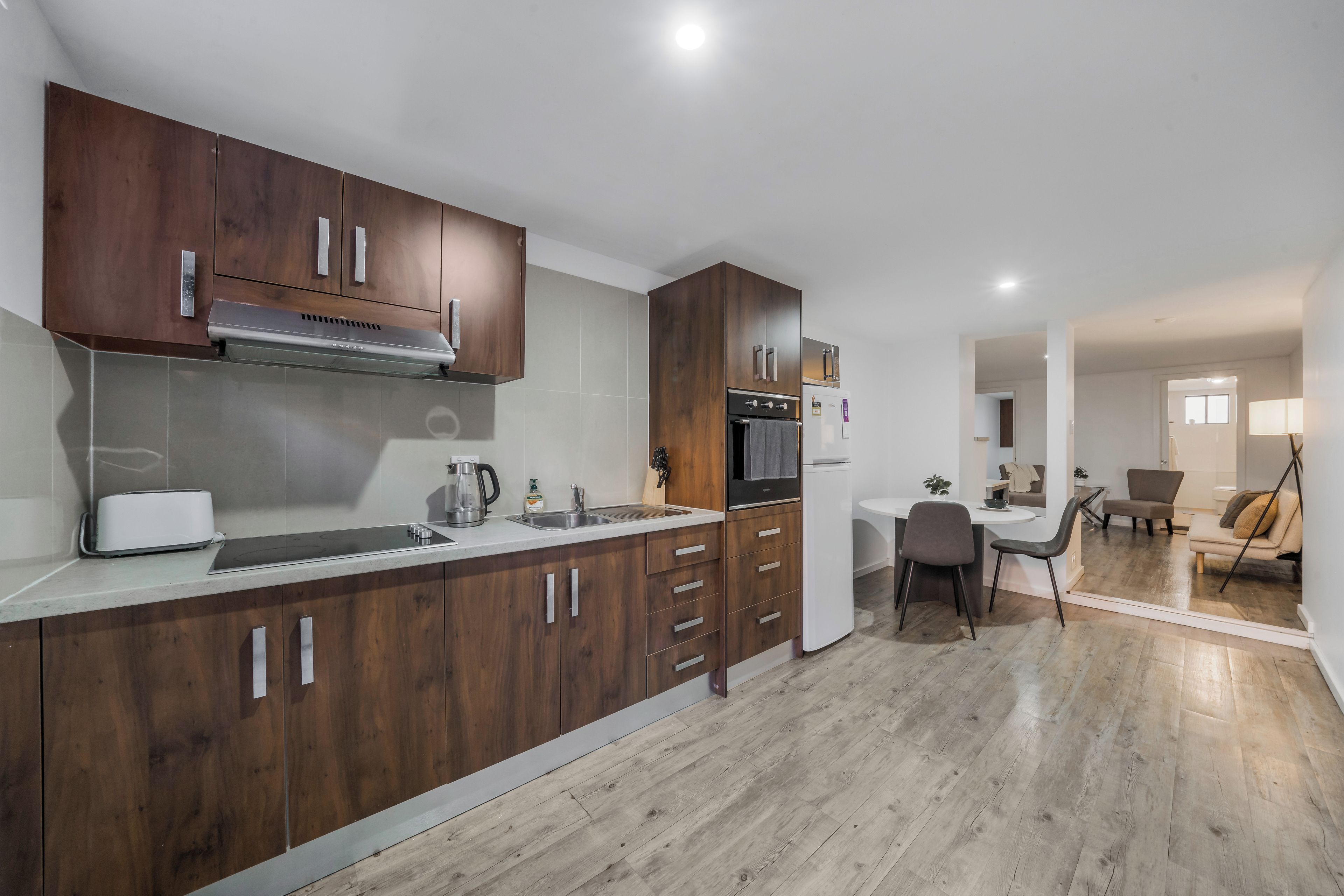 A modern kitchen with wooden cabinets, a built-in oven, and a dining area with a table and chairs.