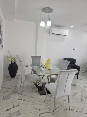 Uma sala de jantar moderna com uma mesa de vidro, cadeiras estofadas cinzas e um vaso com flores.
