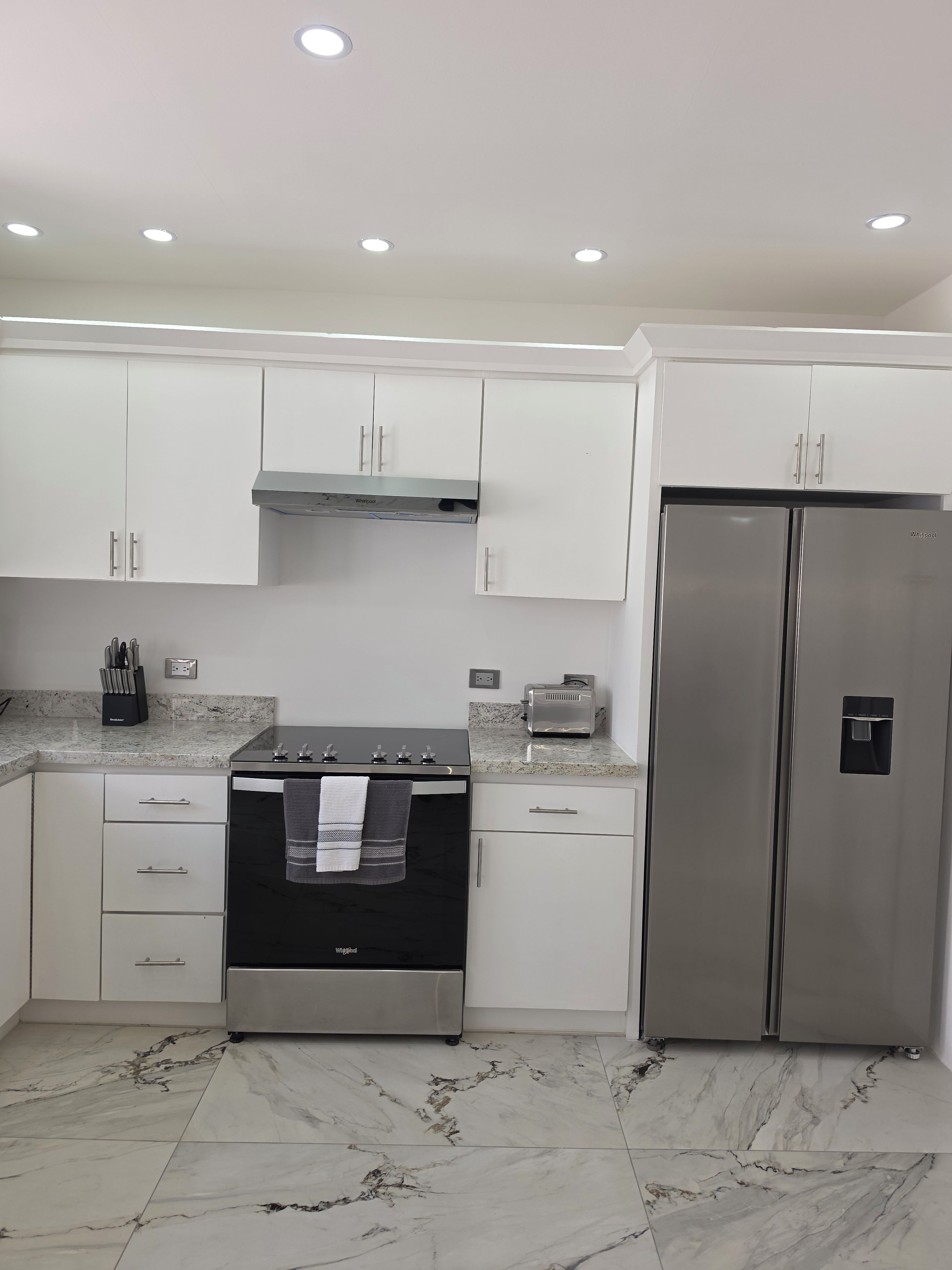 A modern kitchen with white cabinets, a stainless steel refrigerator, a black oven, and a granite countertop.
