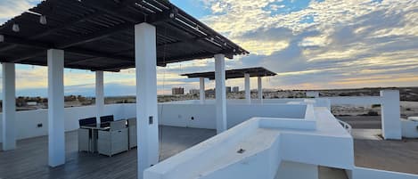 Een terras buiten met een pergola, zithoek en uitzicht op de stad.