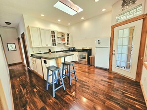 A kitchen with wooden flooring, white cabinets, a central island with stools, and a refrigerator.