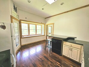 Une cuisine avec un plancher en bois, un réfrigérateur, un lave-vaisselle et une fenêtre donnant sur un espace verdoyant.