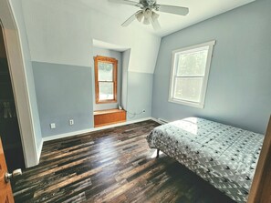 Une chambre à coucher comprenant un lit, une fenêtre, une banquette intégrée et un ventilateur de plafond.