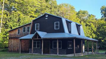 A two-story wooden building with a metal roof, surrounded by trees.