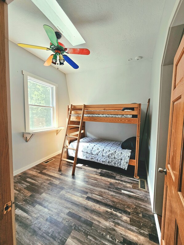 A room with a bunk bed, a window, a ceiling fan, and a door.