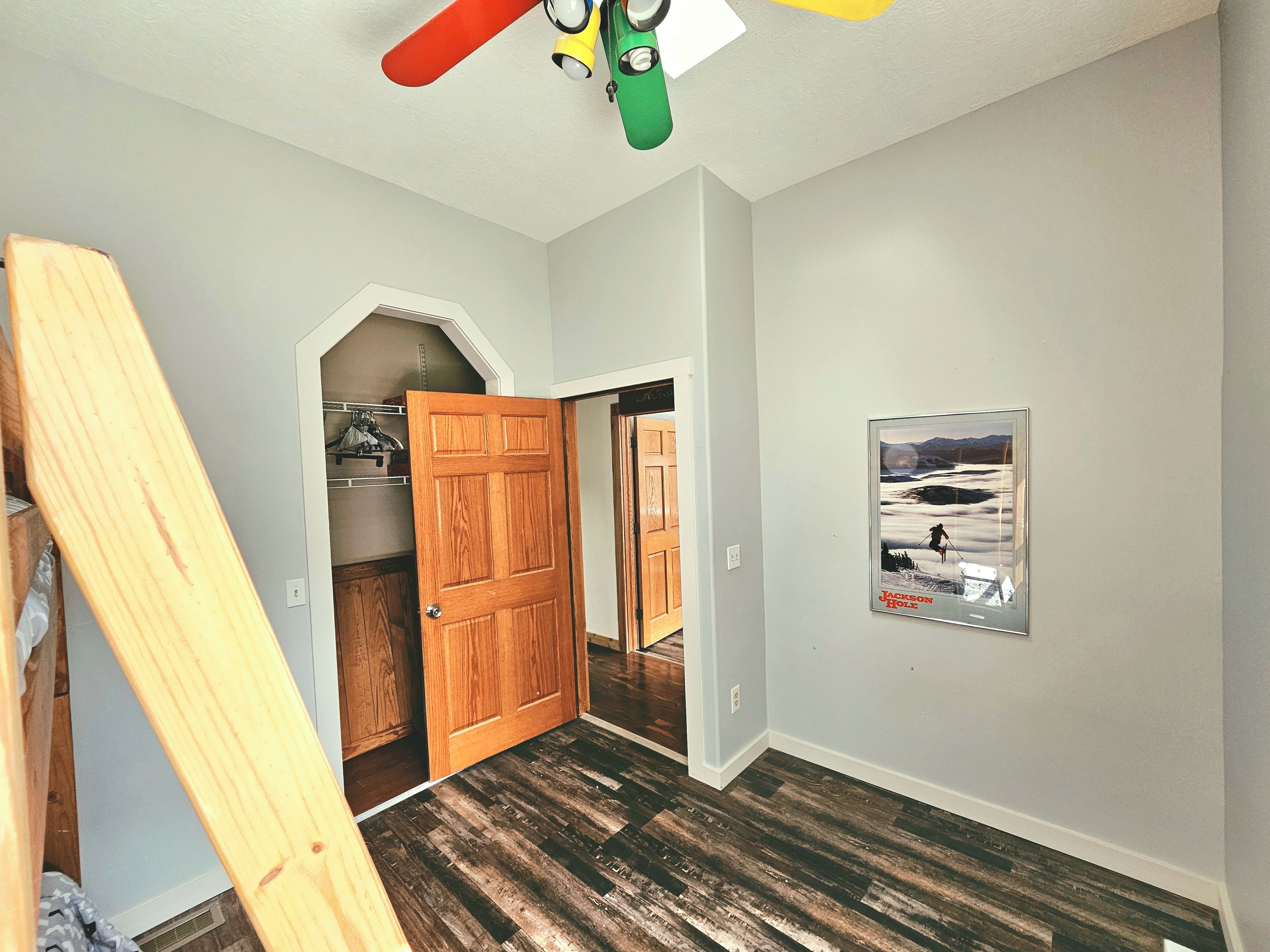 Ein Zimmer mit einer Holztür, einem Poster an der Wand und einem Deckenventilator.