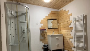 Baño con cabina de ducha de vidrio, panel de pared de madera, lavamanos blanco y toallero.