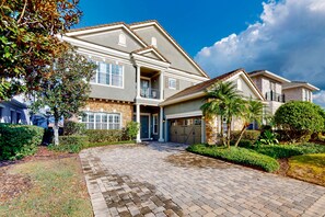 A two-story house with a covered driveway, a garage, and a landscaped garden. - Gorgeous Golf-view Villa With Galactic Themed Bedroom at Reunion (Kissimmee)