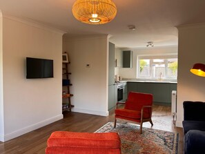 A modern living room with a flat-screen TV, a red chair, and a patterned rug. - The Bungalow Heacham (Heacham)