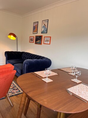 A modern living room with a round dining table, a dark blue sofa, a red armchair, and a floor lamp. - The Bungalow Heacham (Heacham)