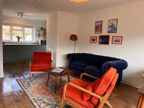 A living room with a blue sofa, red chairs, a coffee table, and a rug. - The Bungalow Heacham (Heacham)