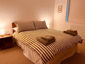 Una cama bien hecha con ropa de cama a rayas y dos almohadas, una mesita de noche con una lámpara y un cuadro en la pared.
