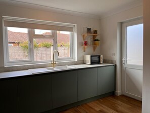 A kitchen with a window, a microwave, and a sink. - The Bungalow Heacham (Heacham)