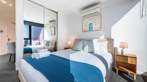 A hotel room with a large bed, a desk, a chair, a bedside table with a lamp, and a wall-mounted air conditioning unit. - Cloud 45 City Views in Southbank (Southbank)