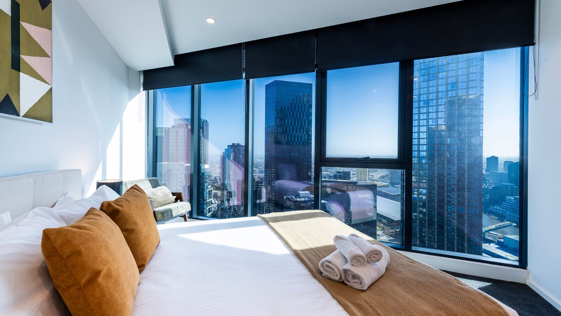 A hotel room with a large bed, a view of the cityscape through floor-to-ceiling windows, and a city skyline in the background.