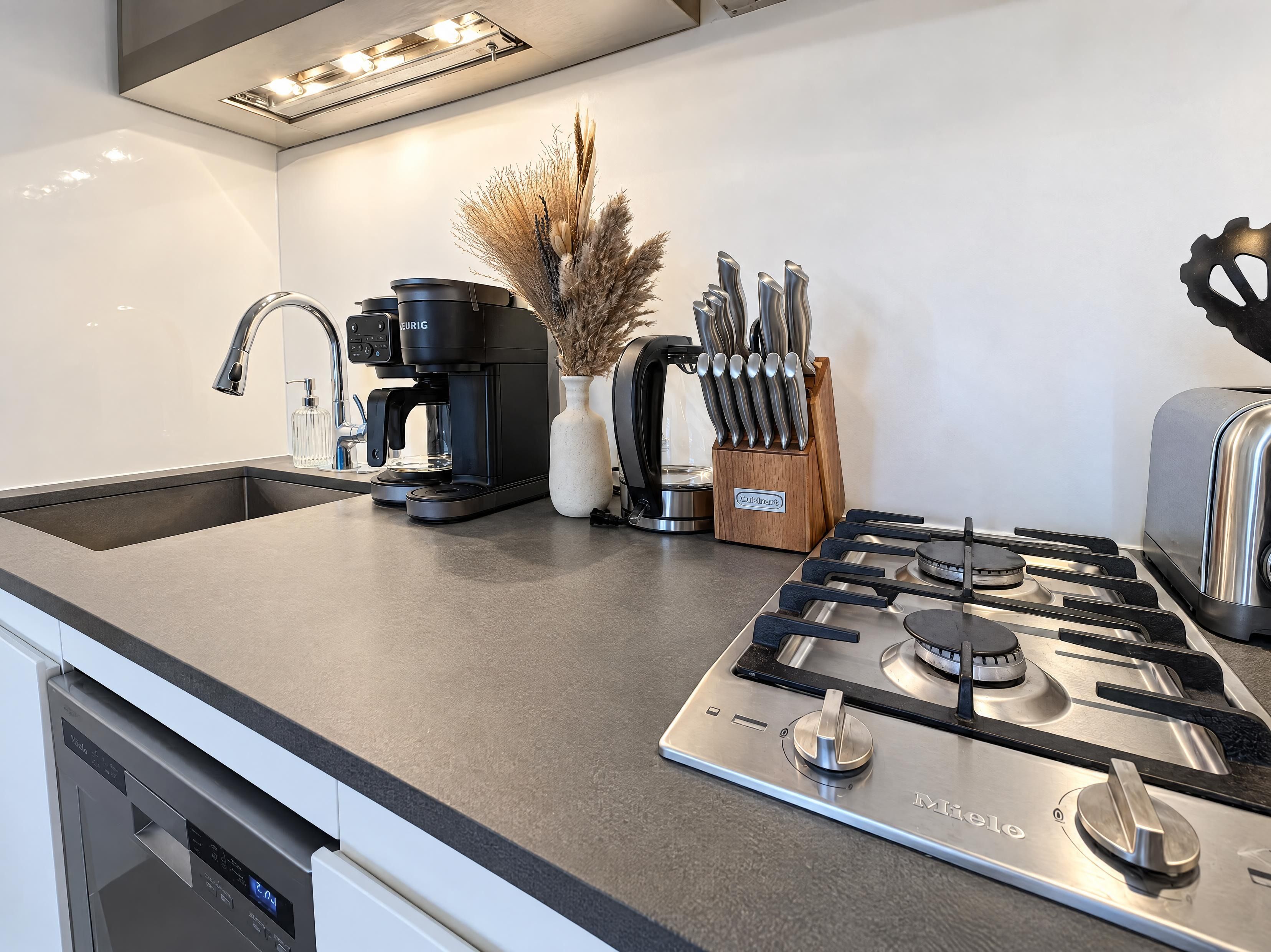A modern kitchen with a built-in dishwasher, a coffee maker, a gas stove, and a toaster.
