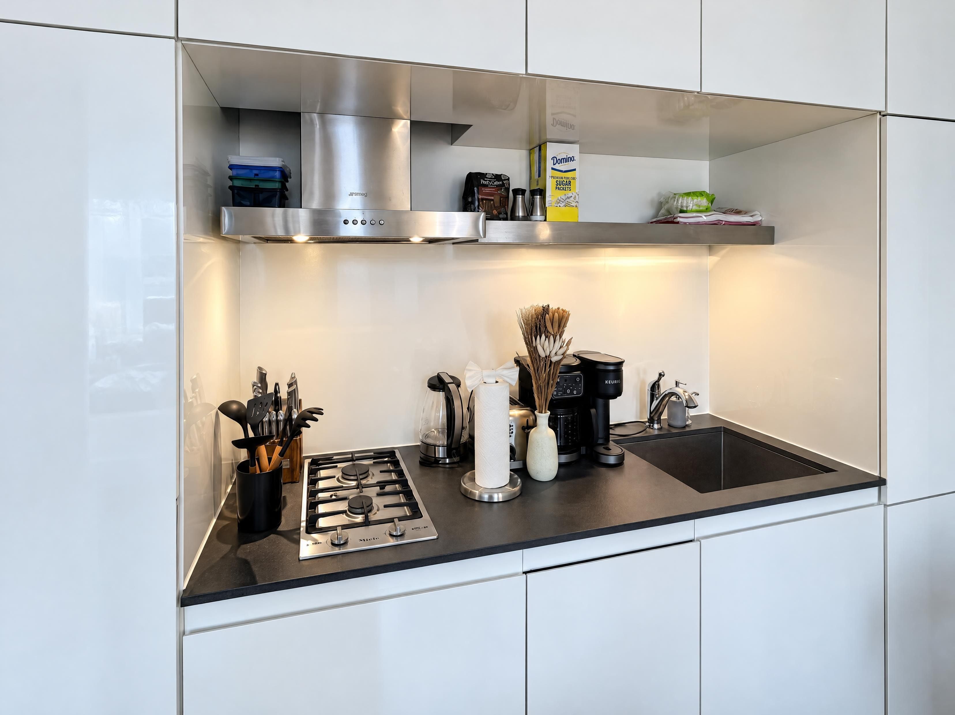 A modern kitchen with a gas stove, coffee maker, and a box of Domino sugar packets.