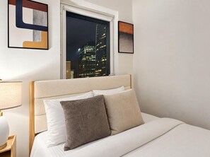 Habitación de hotel con una cama, vista nocturna de un paisaje urbano y un cuadro abstracto enmarcado en la pared.